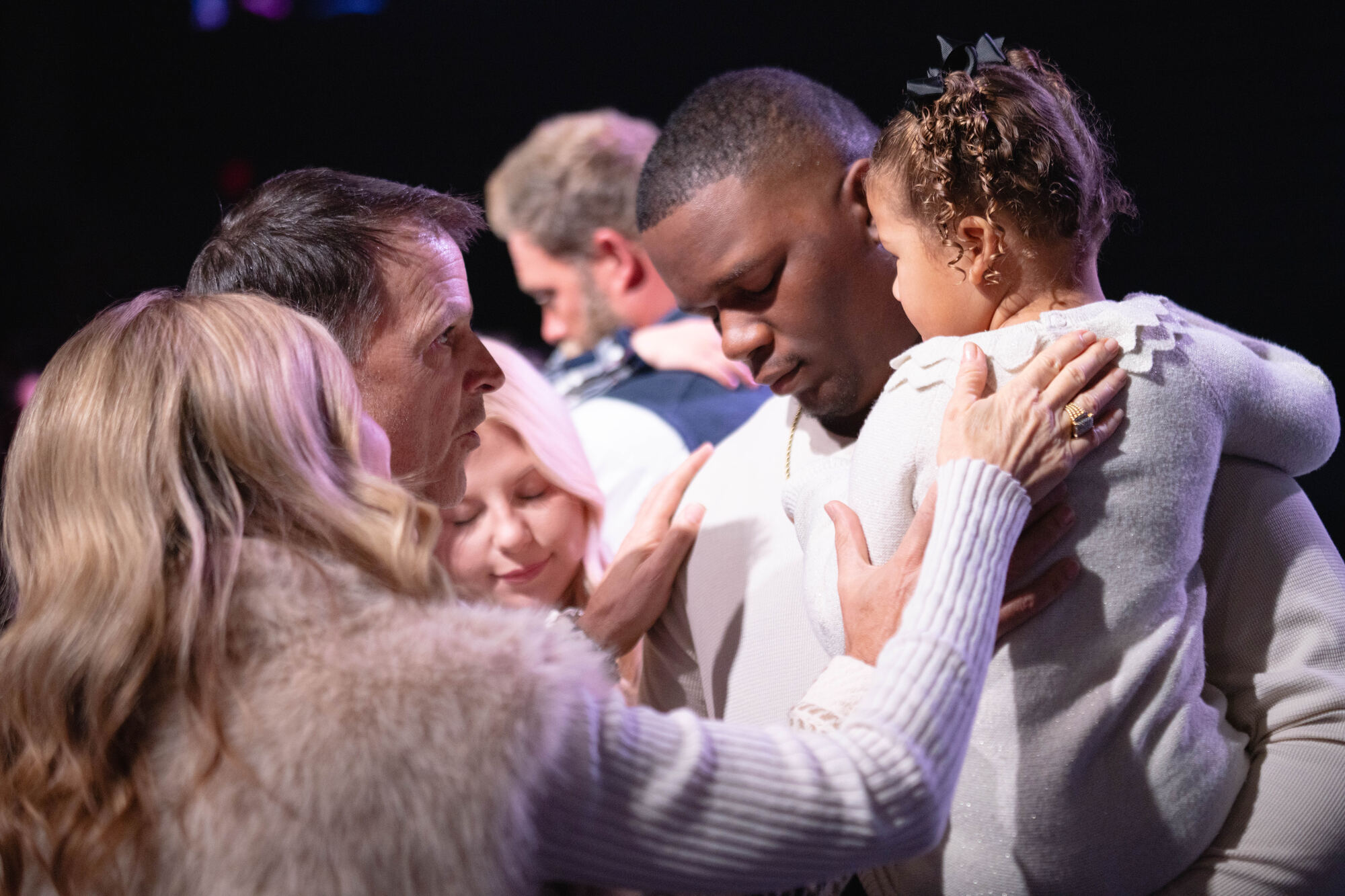 Pastors praying over a father holding his daughter during a dedication service