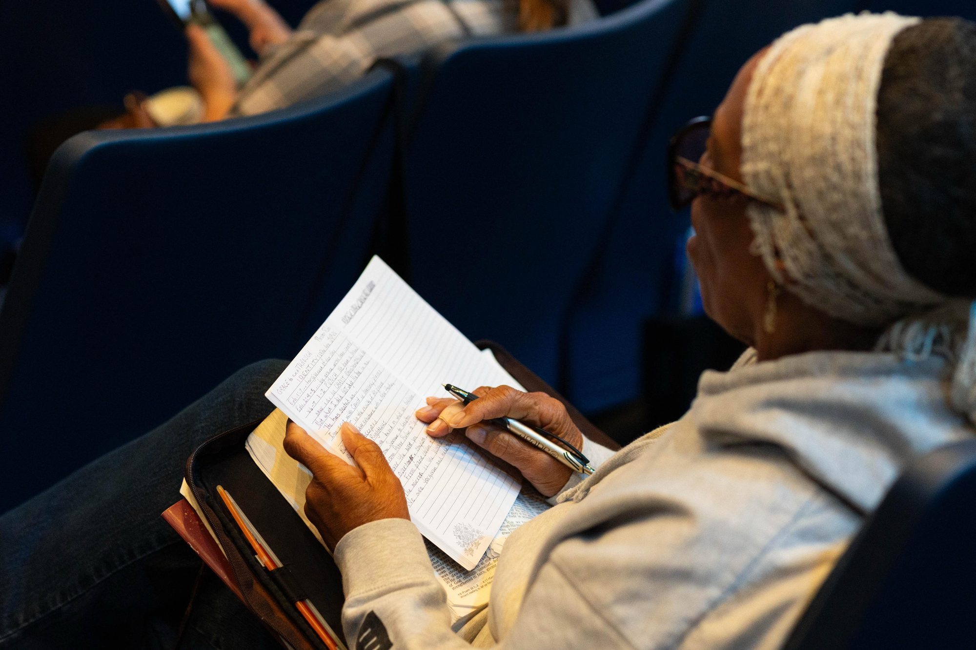 A woman taking notes in her journal beside an open Bible during a service