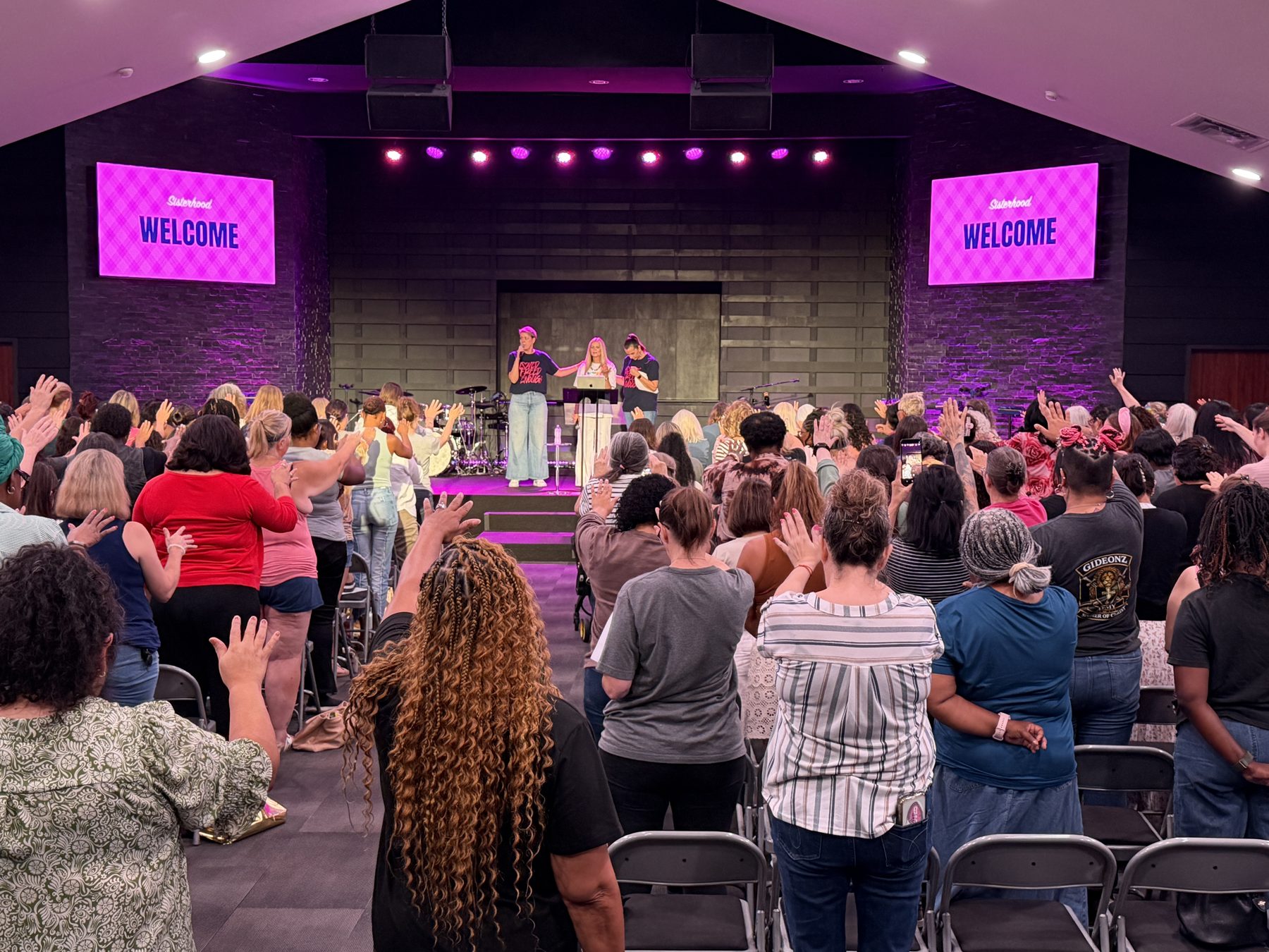 Women worshipping together with hands raised at a Sisterhood night