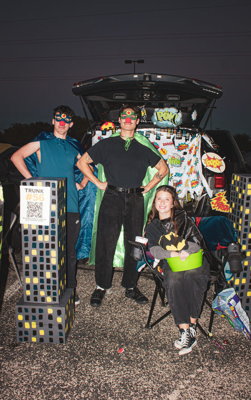 Three students at a comic-book trunk with painted city skyscrapers
