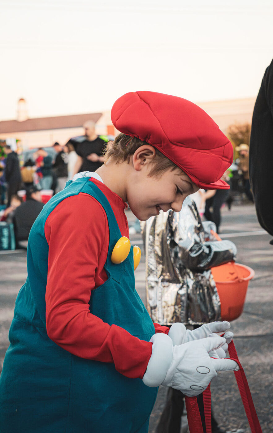 A boy in a red cap and dungarees looking into his candy bag